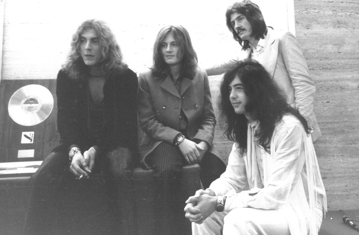 The members of Led Zeppelin look off-camera with a gold record next to them