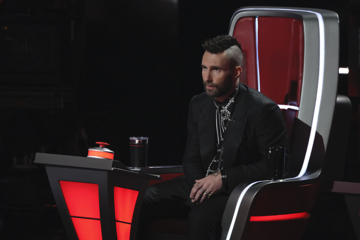 Adam Levine sits in the coach's chair in a black suit on 'The Voice'