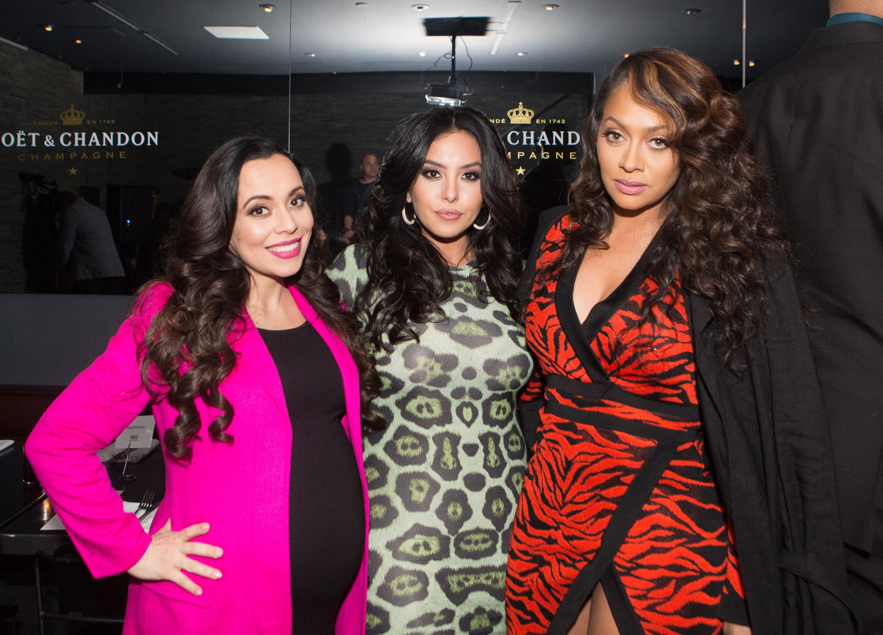 Adrienne Bosh hugging Vanessa Bryant and La La Anthony while wearing bright and patterned dresses.