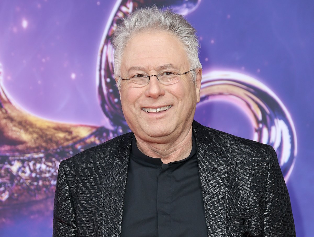 Alan Menken in a black and silver suit in front of a purple backdrop at the live-action 'Aladdin' premiere