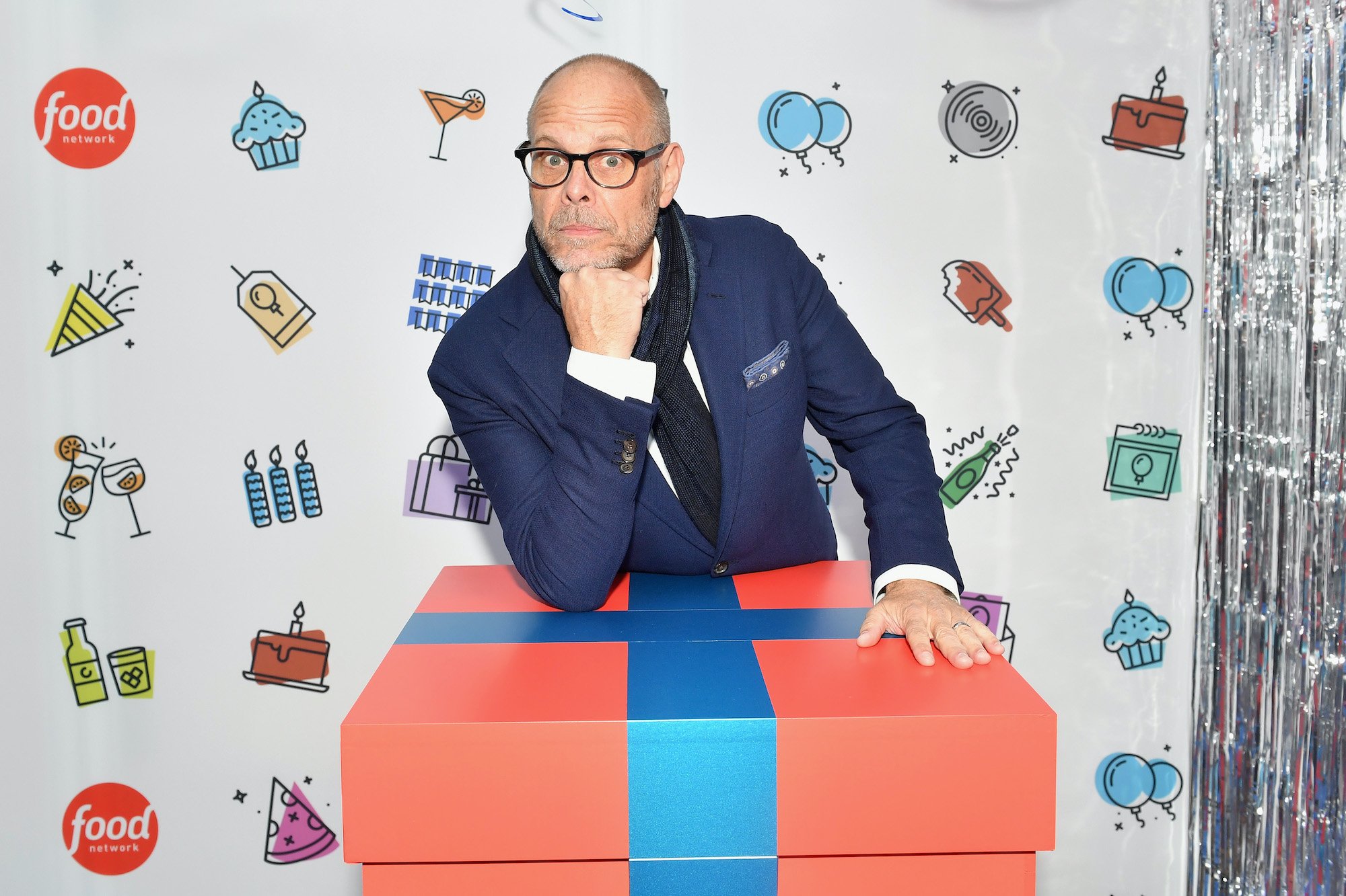 Alton Brown smiling in front of a white backdrop