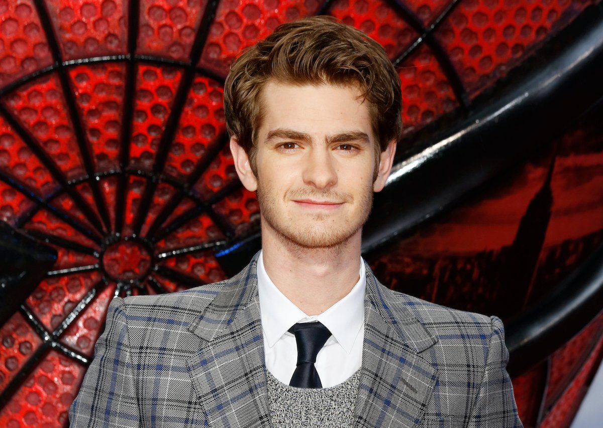 Andrew Garfield in a grey checkered suit standing in front of a Spider-Man backdrop at the Berlin premiere of 'The Amazing Spider-Man' in June 2012