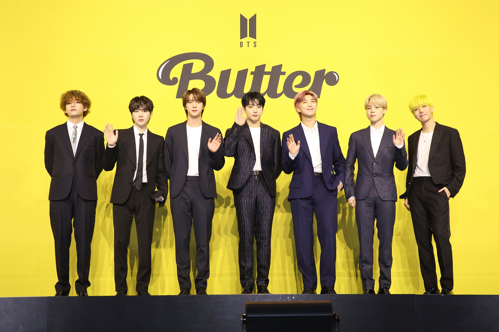 V, Suga, Jin, Jungkook, RM, Jimin, and J-Hope of BTS pose in front of a yellow backdrop at the band's press conference for their song 'Butter'