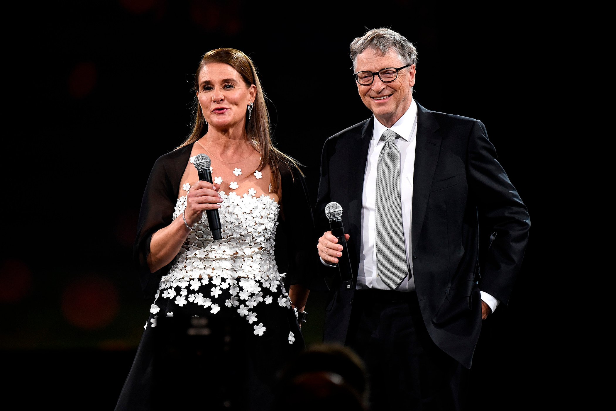 Melinda Gates and Bill Gates speaking to a crowd against a black background