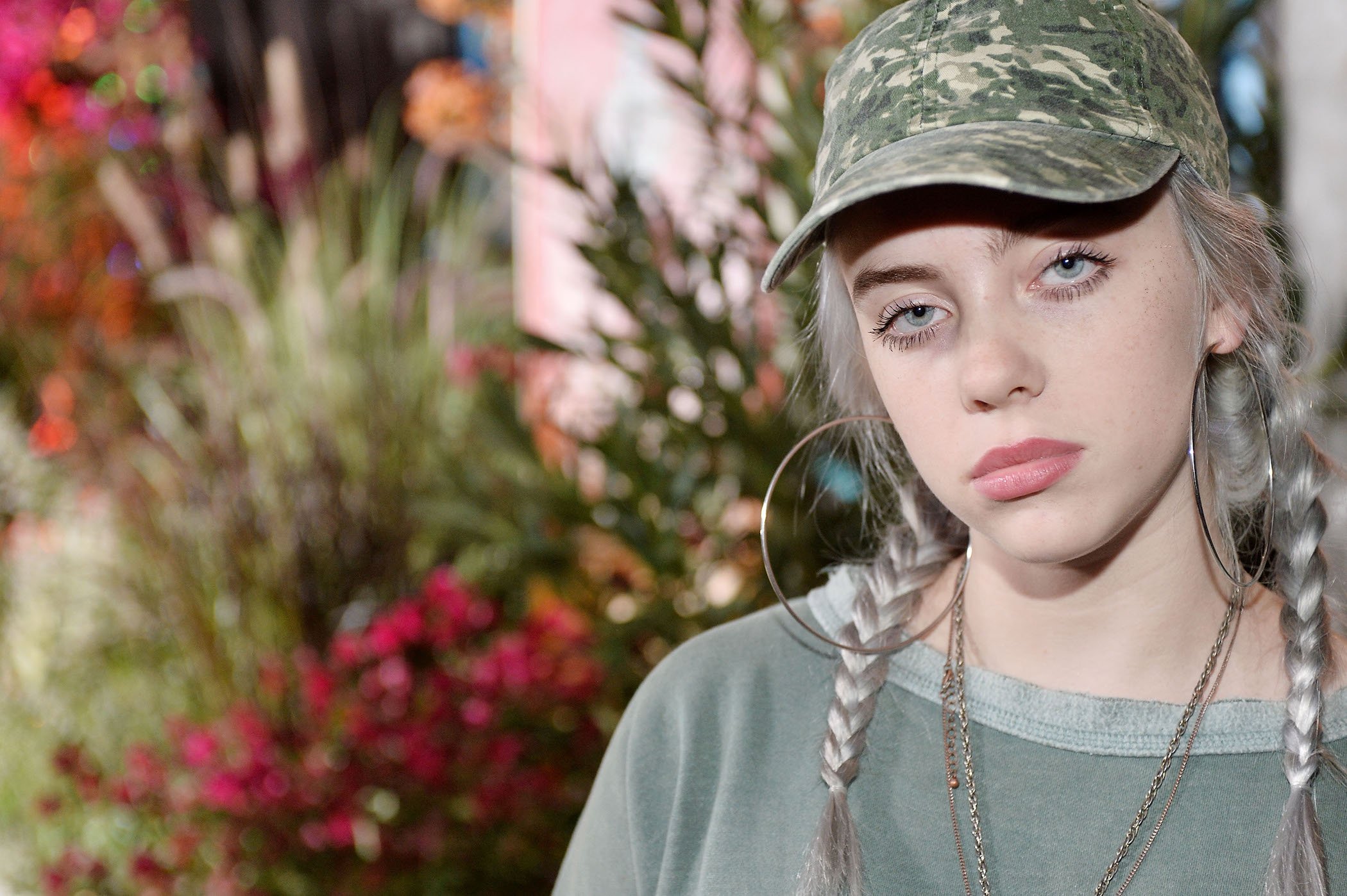 A close-up of Billie Eilish wearing a camo hat and a green shirt at a Teen Vogue event