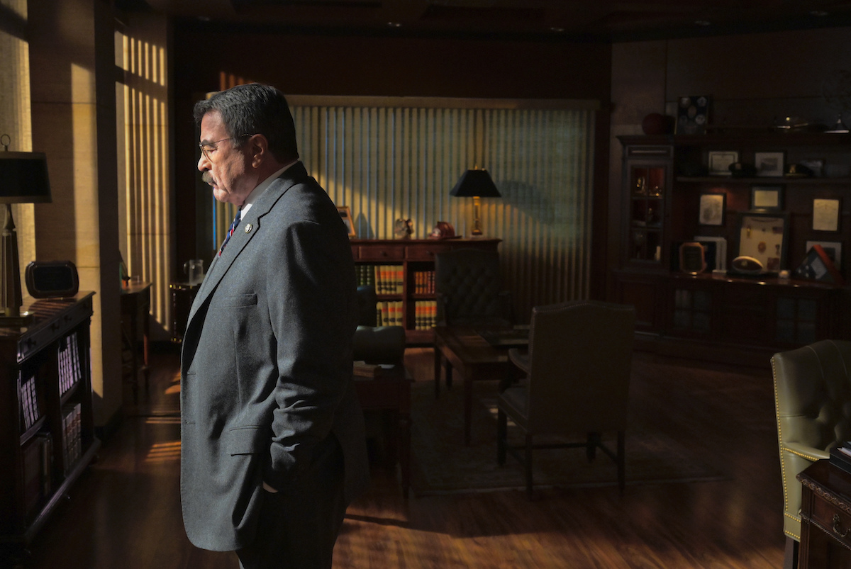 Tom Selleck as Frank Reagan stands in his office in front of a window in 'Blue Bloods'