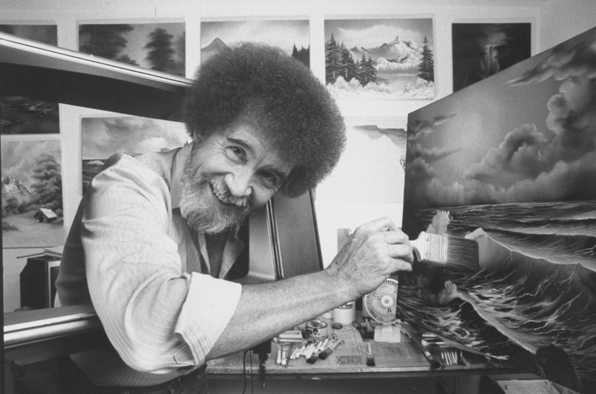TV painting instructor/artist Bob Ross using a large paint brush to touch up one of his large seascapes in his studio at home.  