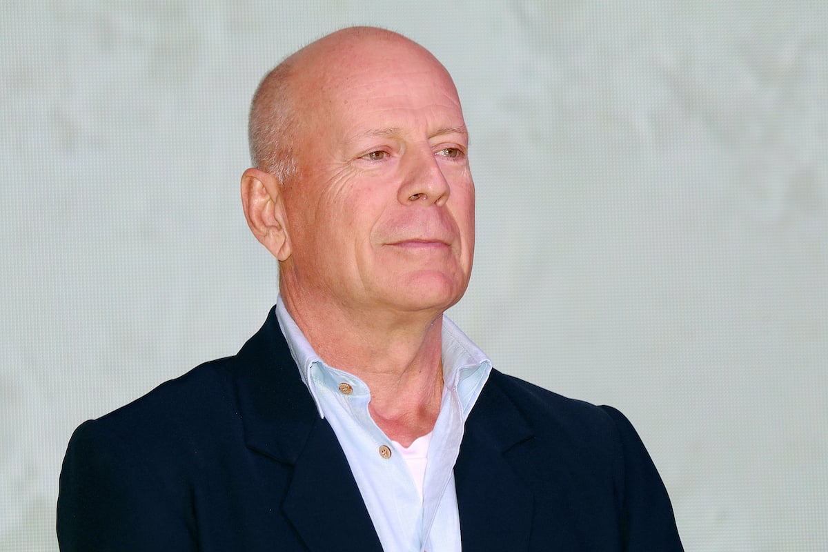 Bruce Willis poses in a light collared shirt and dark jacket in 2019