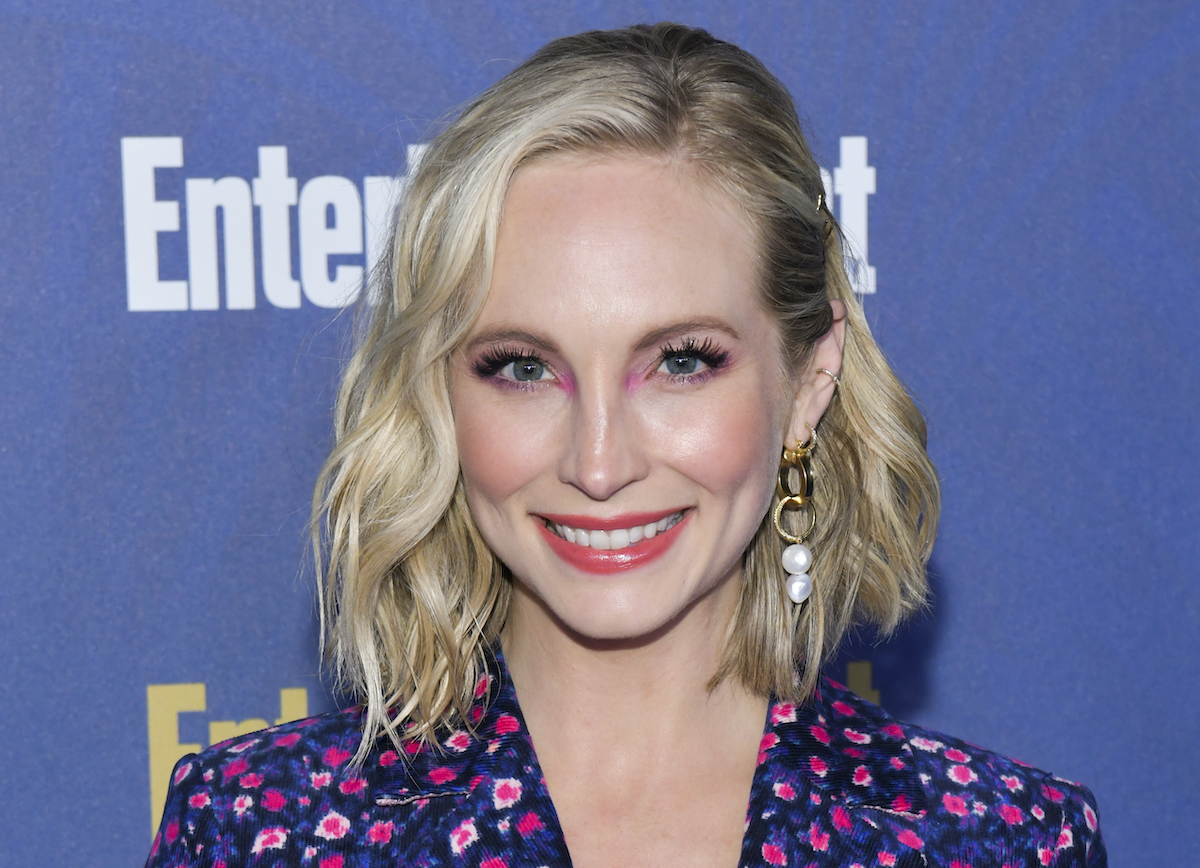 Candice King in a blue and pink floral suit smiling in front of a blue backdrop