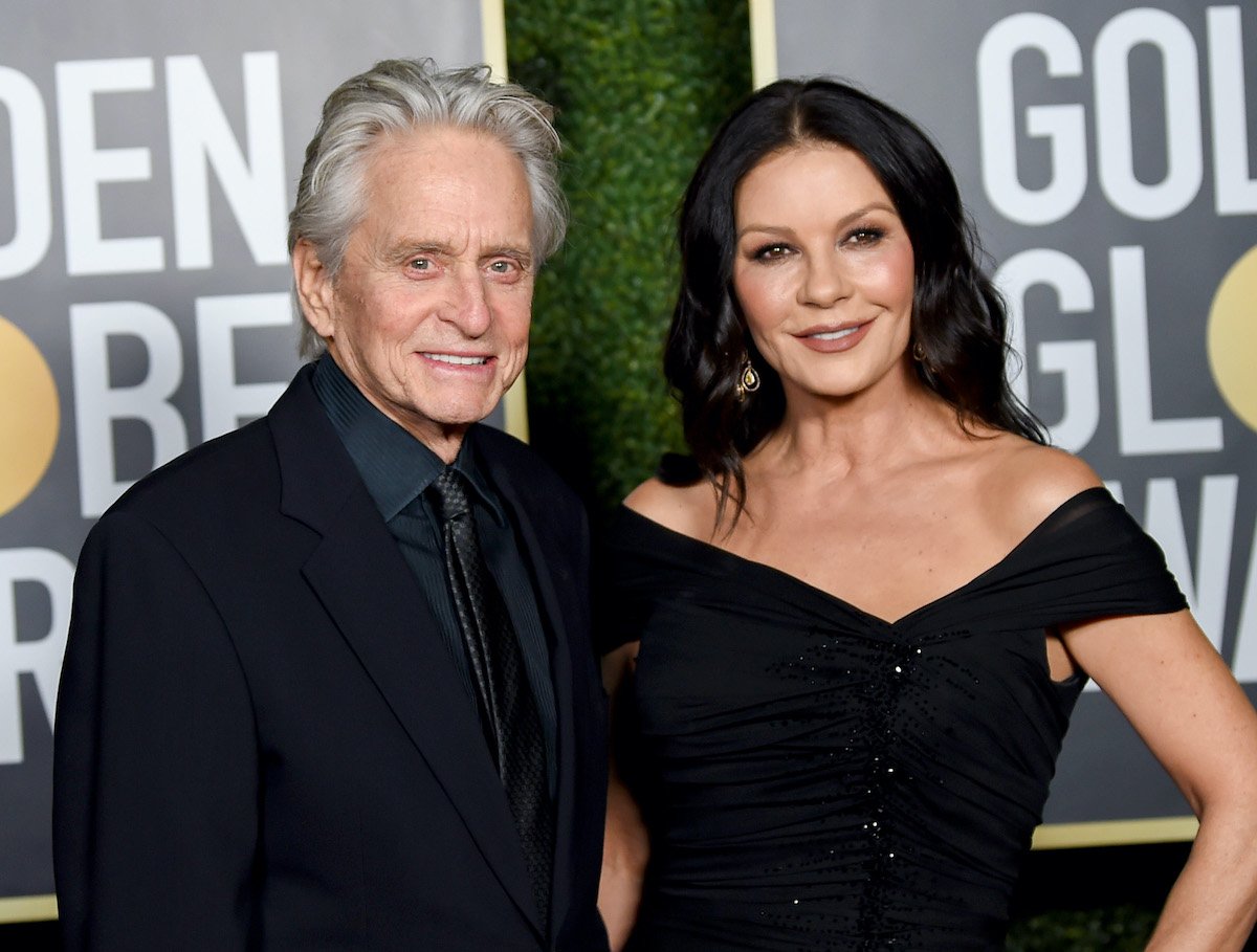 Michael Douglas in a black suit and Catherine Zeta-Jones in a black gown while smiling on the red carpet of the 2021 Golden Globe Awards