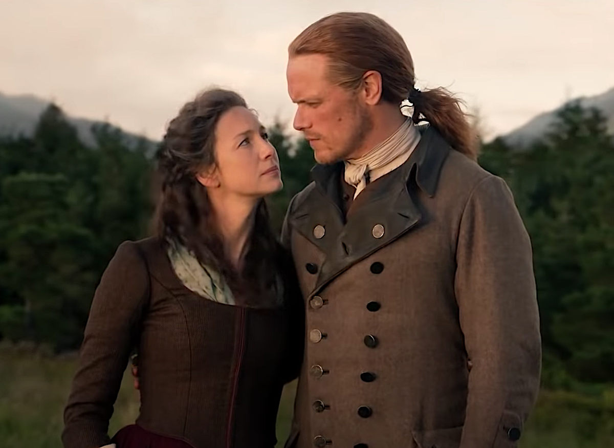 Caitriona Balfe wearing a brown long-sleeved dress as Claire and Sam Heughan in a brown coat with brass buttons and black lapels as Jamie in 'Outlander'