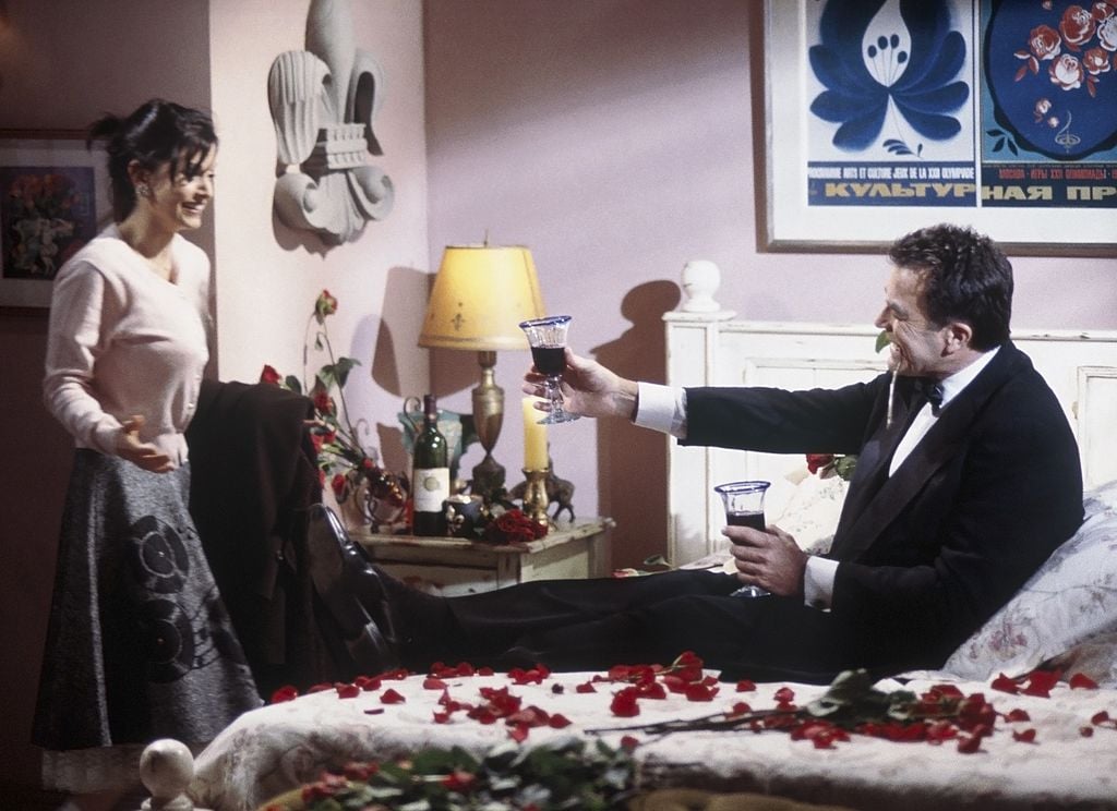 Courteney Cox Arquette as Monica Gelle walks into the room where Tom Selleck as Dr. Richard Burke sits on a bed of roses.