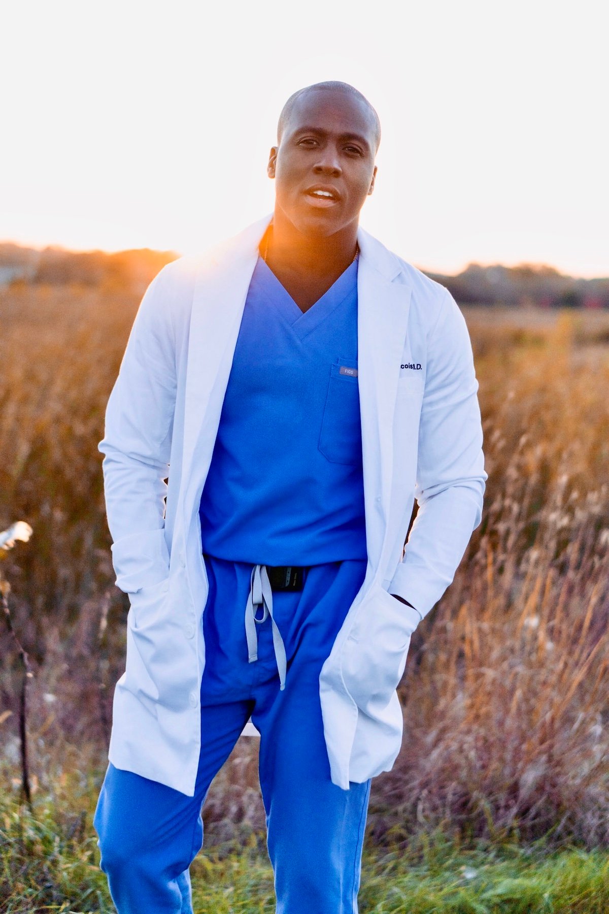 Dr. Elvis Francois, 'The Singing Surgeon' from The Masked Singer wearing a white coat and standing in a field