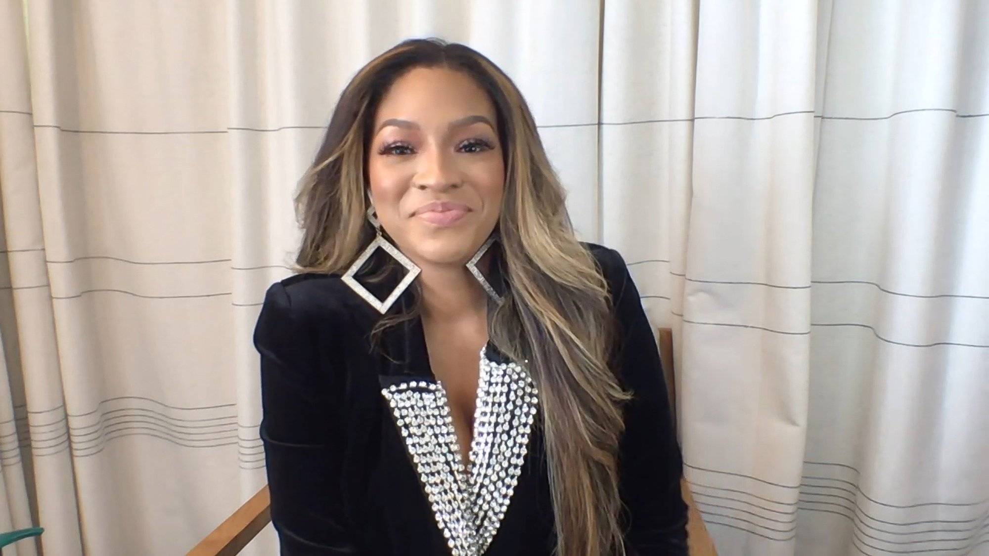 Drew Sidora smiling in front of a curtain