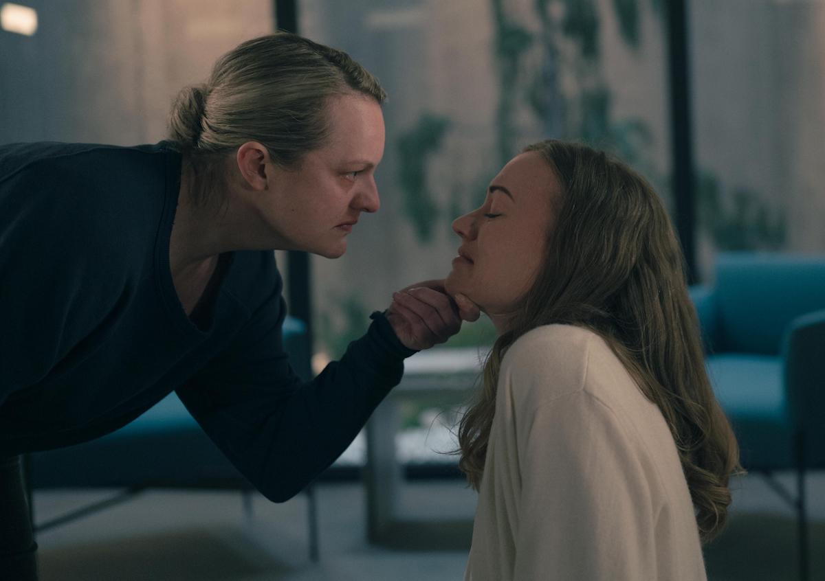 Elisabeth Moss as June looking angry and holding Yvonne Strahovski as Serena Joy Waterford's crying face in her hand in 'The Handmaid's Tale' Season 4. Moss wears a navy blue crew neck and Stahovski wears a cream colored blouse.