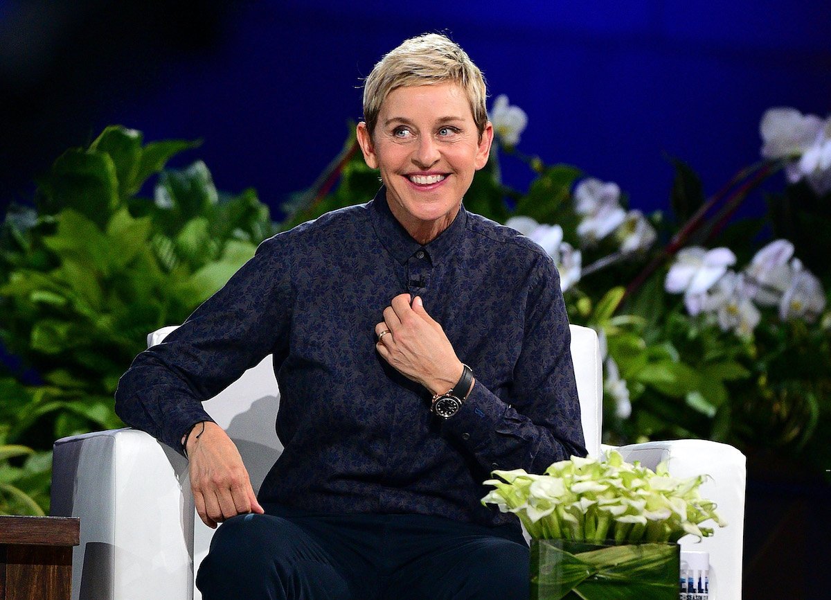 Ellen DeGeneres in a floral navy blue button-down shirt in front of a blue background with green plants behind her