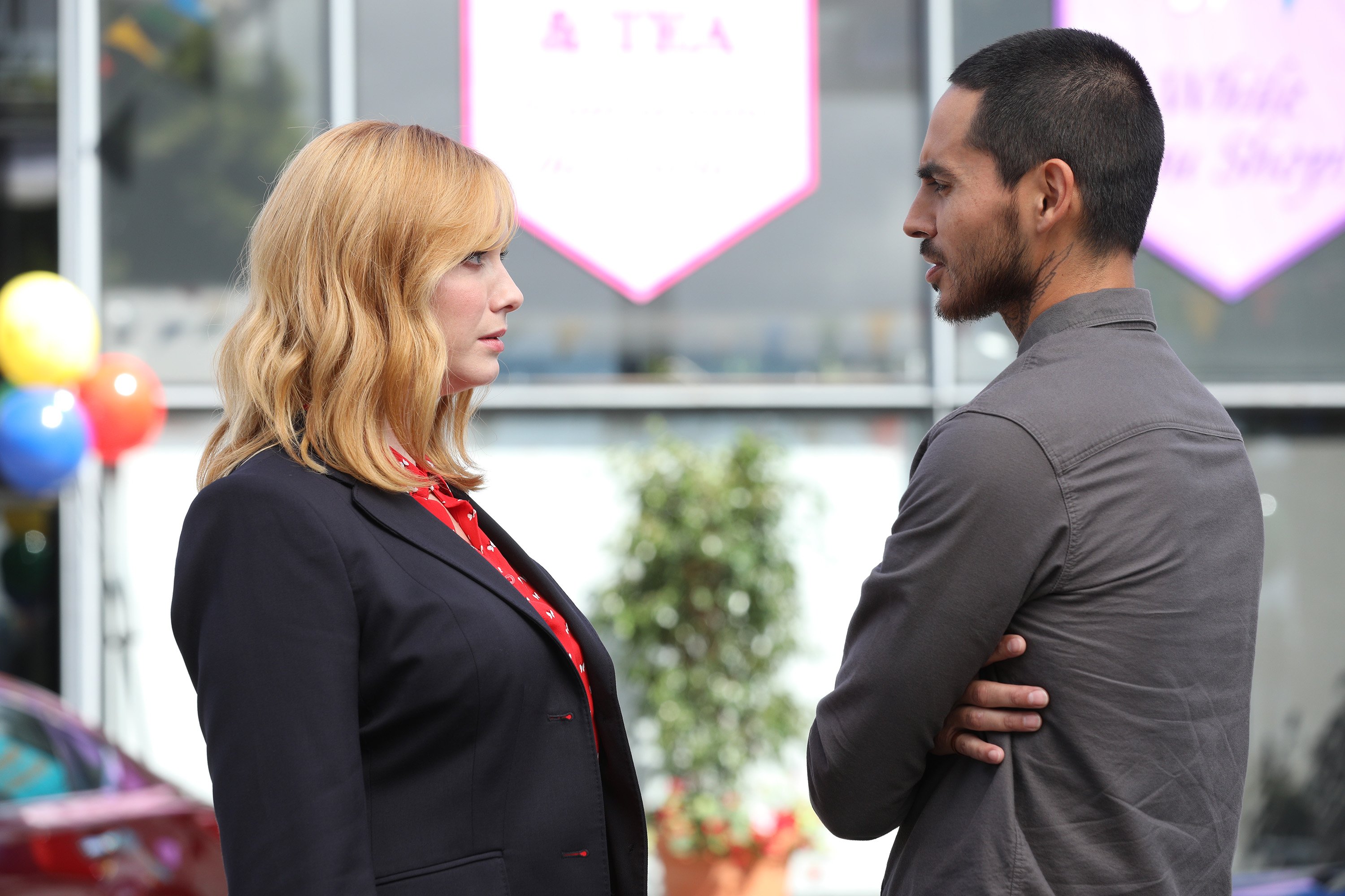'Good Girls': Christina Hendricks at Beth wearing a black blazer and red shirt while speaking to Manny Montana as Rio in a grey shirt.