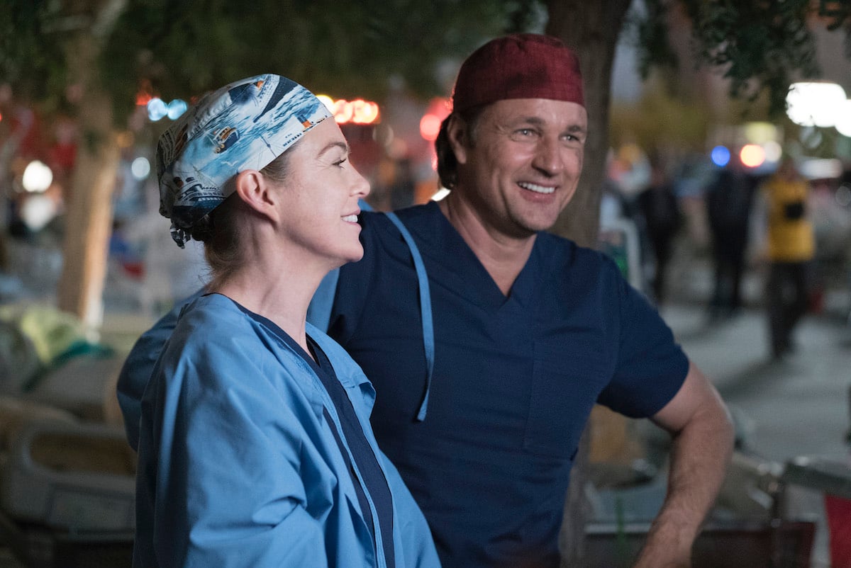 Ellen Pompeo as Meredith Grey and Martin Henderson as Dr. Nathan Riggs are smiling dressed in their scrubs