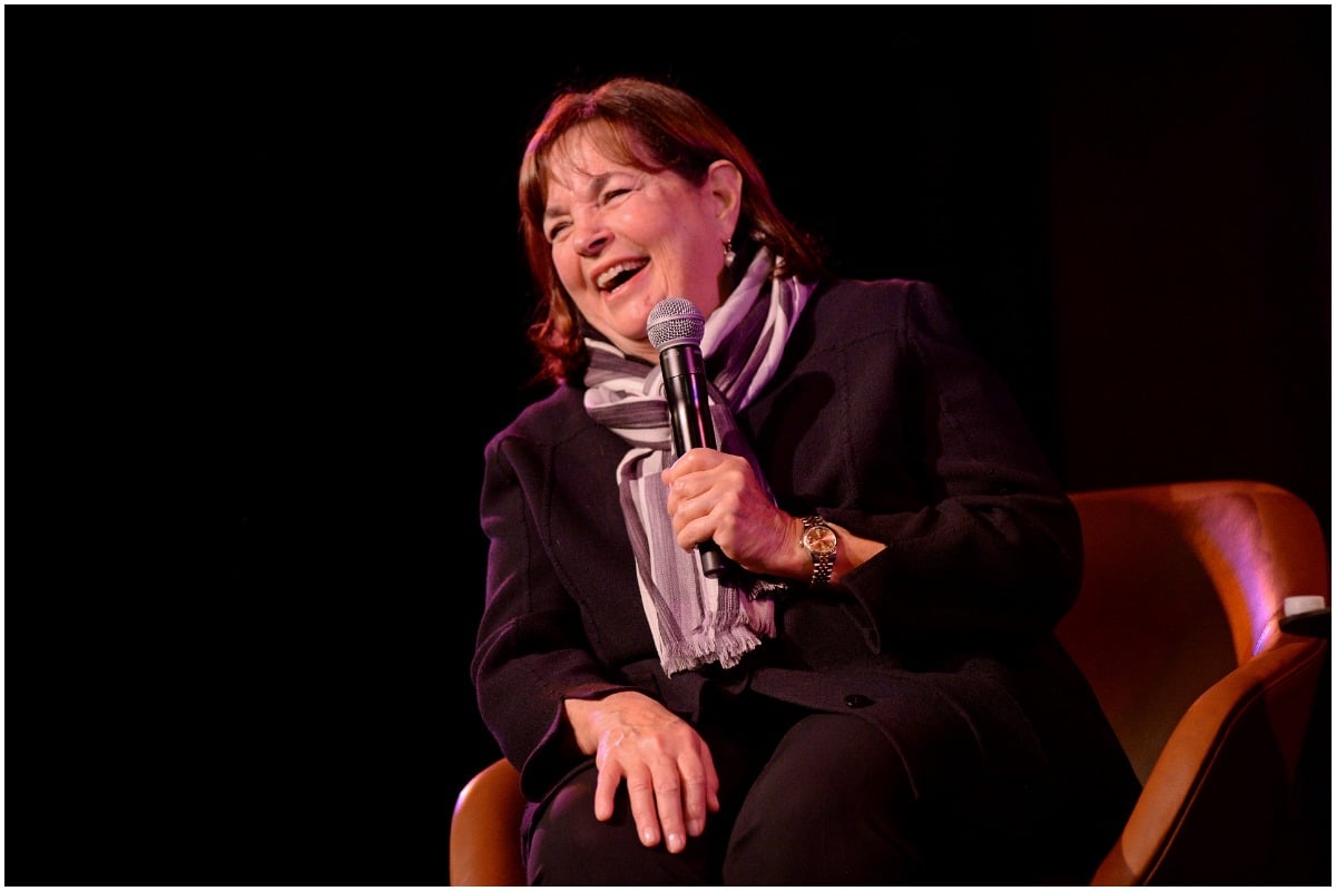 'Barefoot Contessa' star Ina Garten is laughing while wearing an all-black outfit and a pattern scarf. She is holding a microphone onstage.