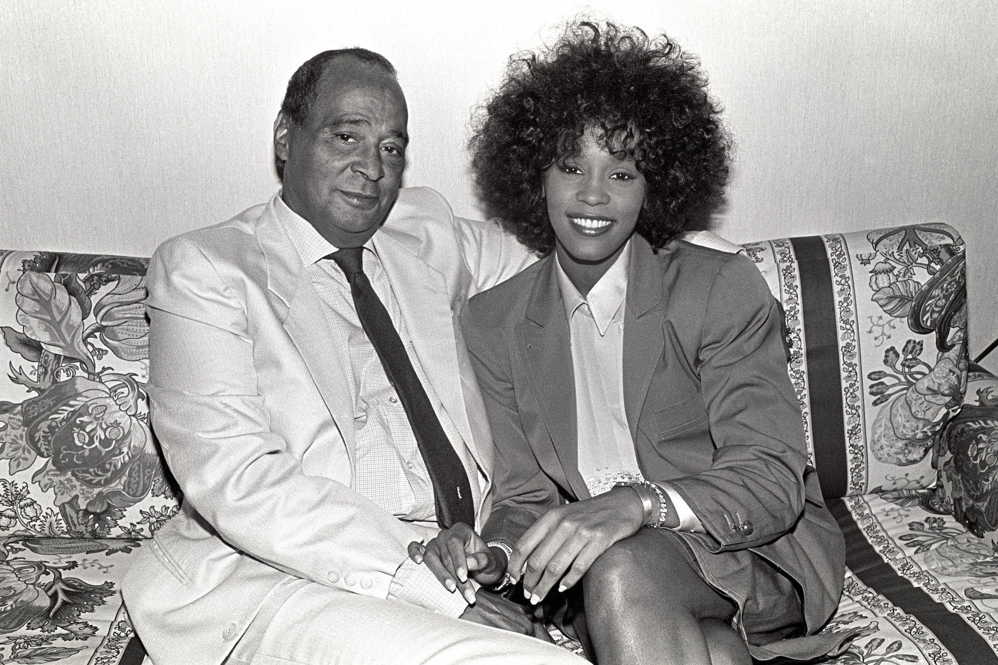 Whitney Houston sits on a sofa with  her father, John Houston