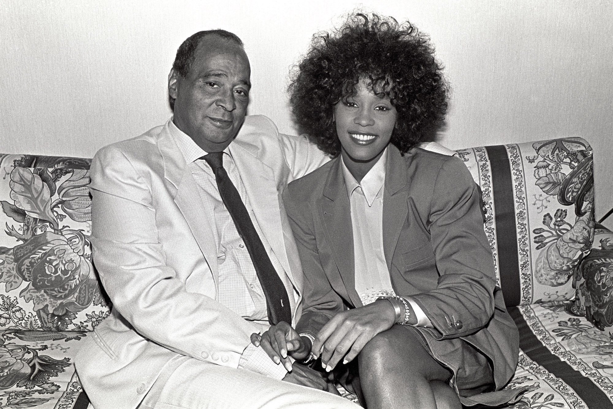 Whitney Houston sits on a sofa with her father, John Houston