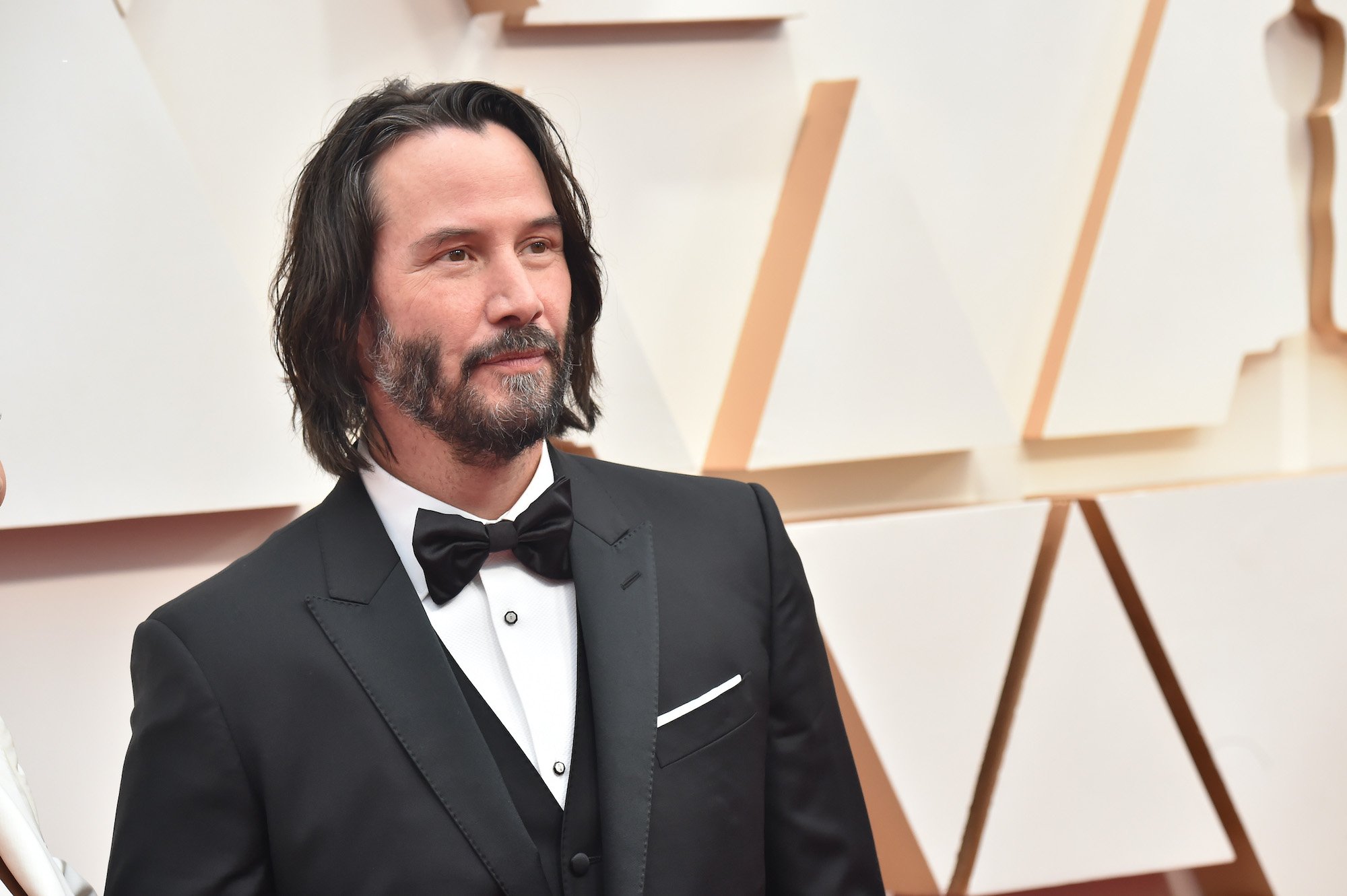 Keanu Reeves smiling in front a white background