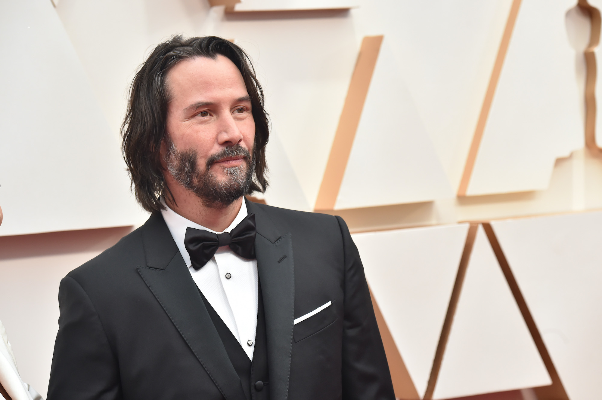 Keanu Reeves smiling in front a white background at the 2020 Oscars