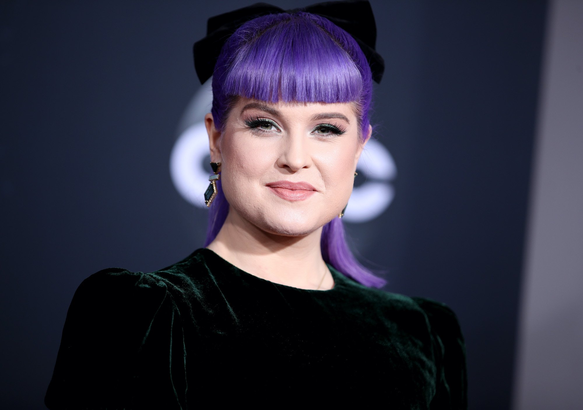Kelly Osbourne smiling in front of a black background
