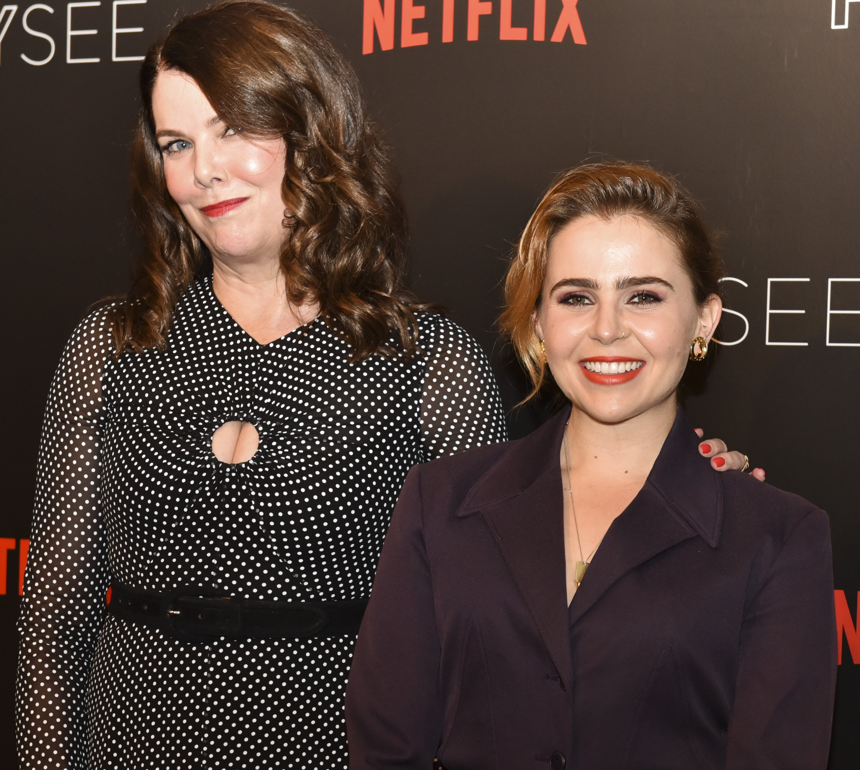 'Good Girls' star Mae Whitman smiling in a black blazer while standing next to her 'Parenthood' co-star, Lauren Graham, who is wearing a black and white polka dot dress.