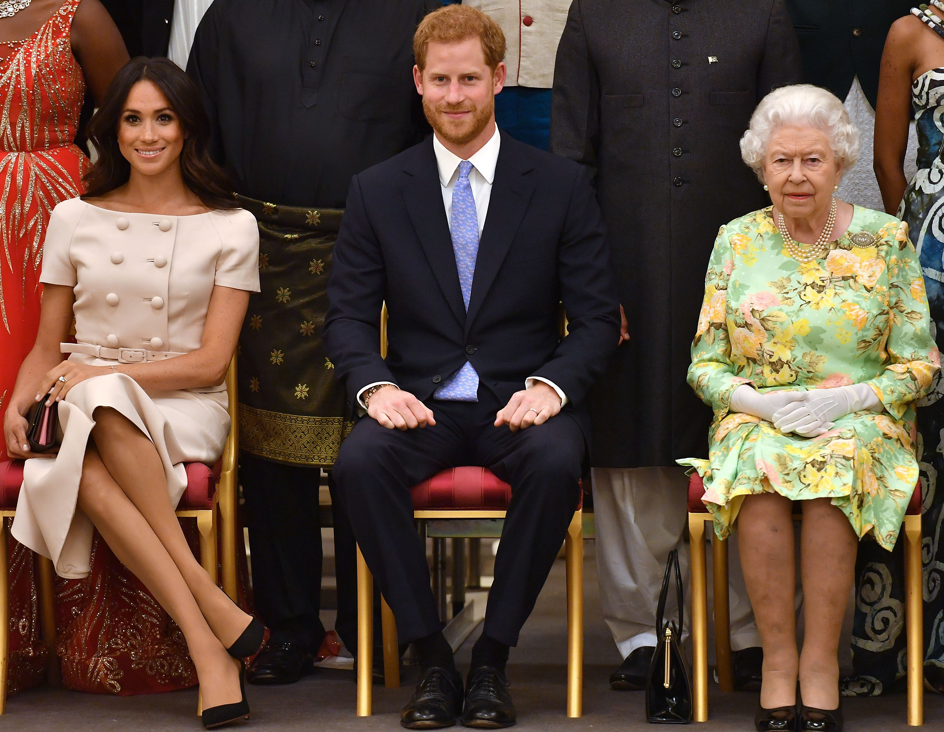 Meghan Markle, Prince Harry, and Queen Elizabeth II seated next to one another and posing for a photo at the Queen's Young Leaders Awards Ceremony