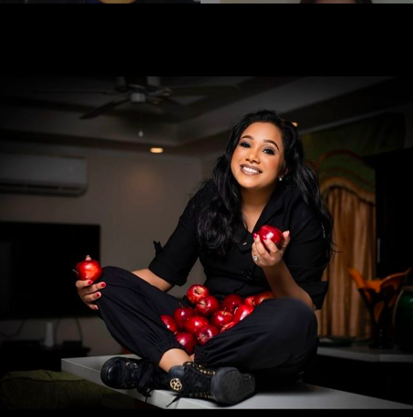 Chef Natasha de Bourg poses with apples while sitting on a table.