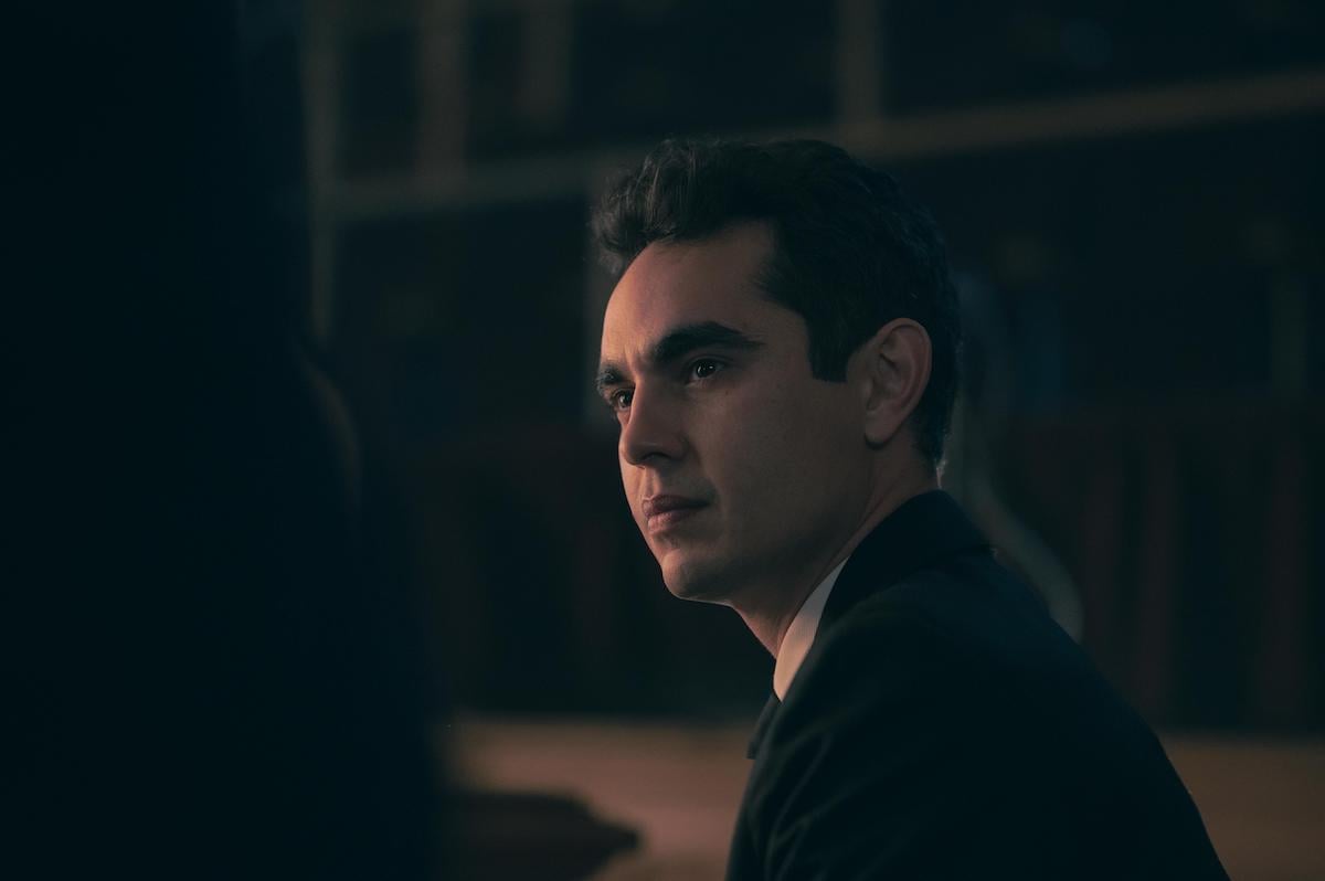 Max Minghella in a black suit and white shirt looking stern in a darkly lit room as Nick in 'The Handmaid's Tale' Season 4.