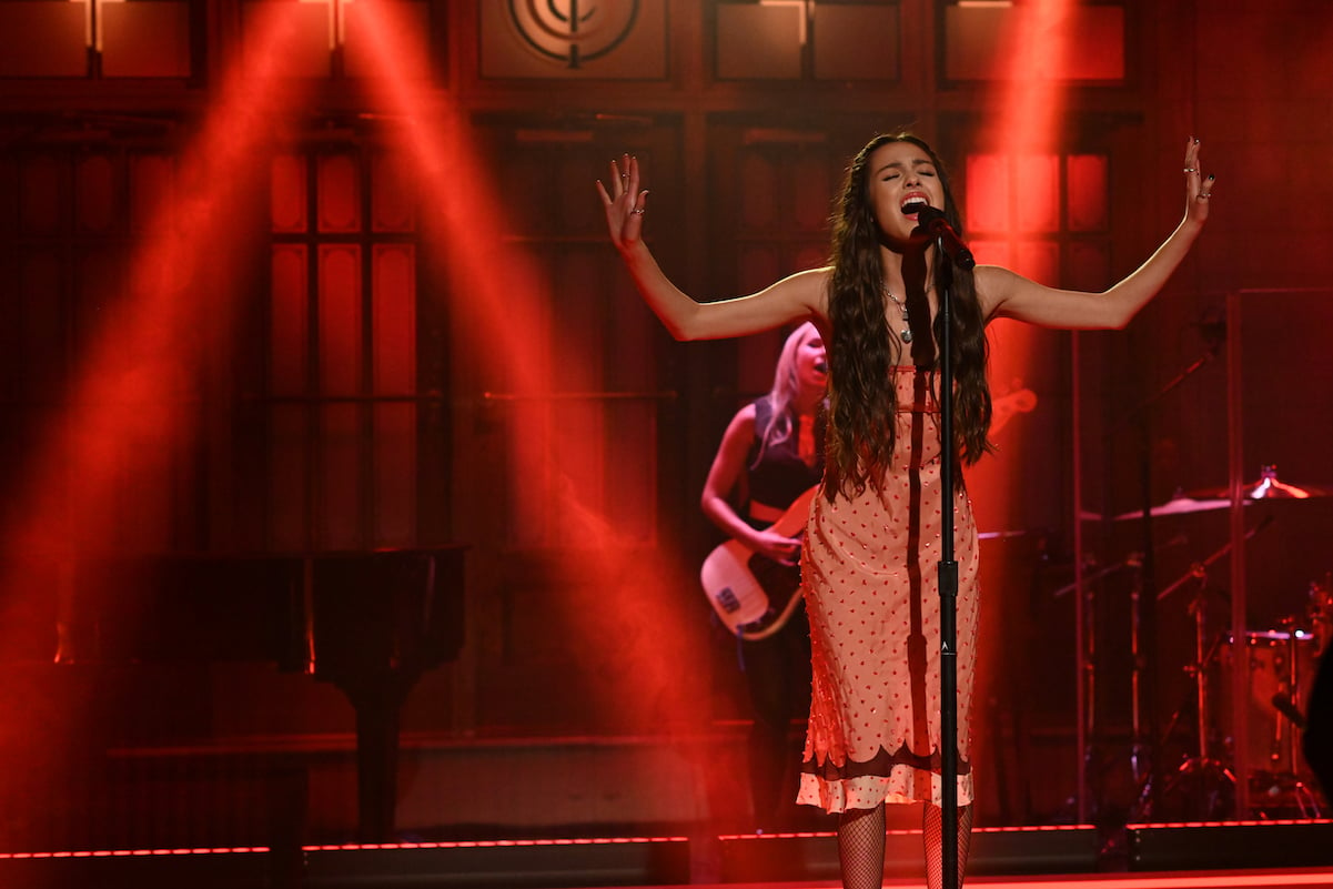 Olivia Rodrigo performing in a pink dress with her arms up on 'SNL'