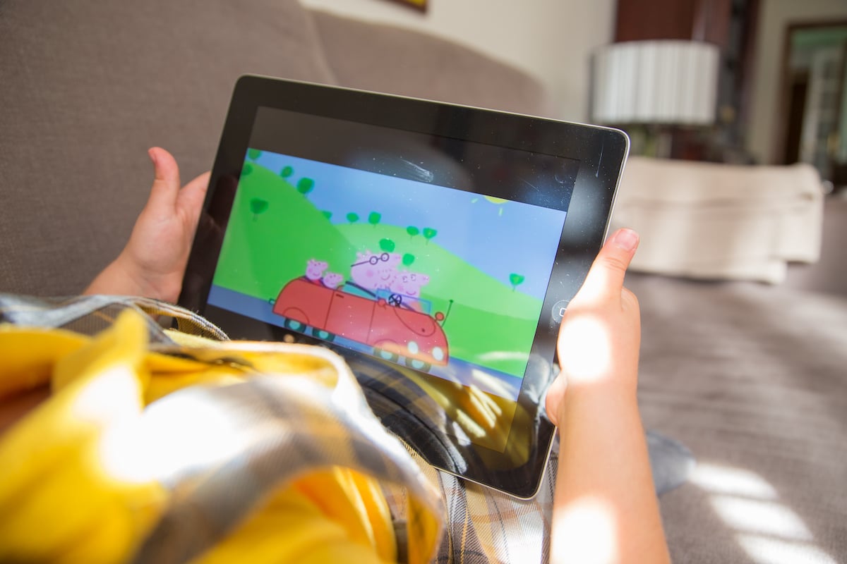 A child watches 'Peppa Pig' on an iPad tablet while lying on a sofa at home