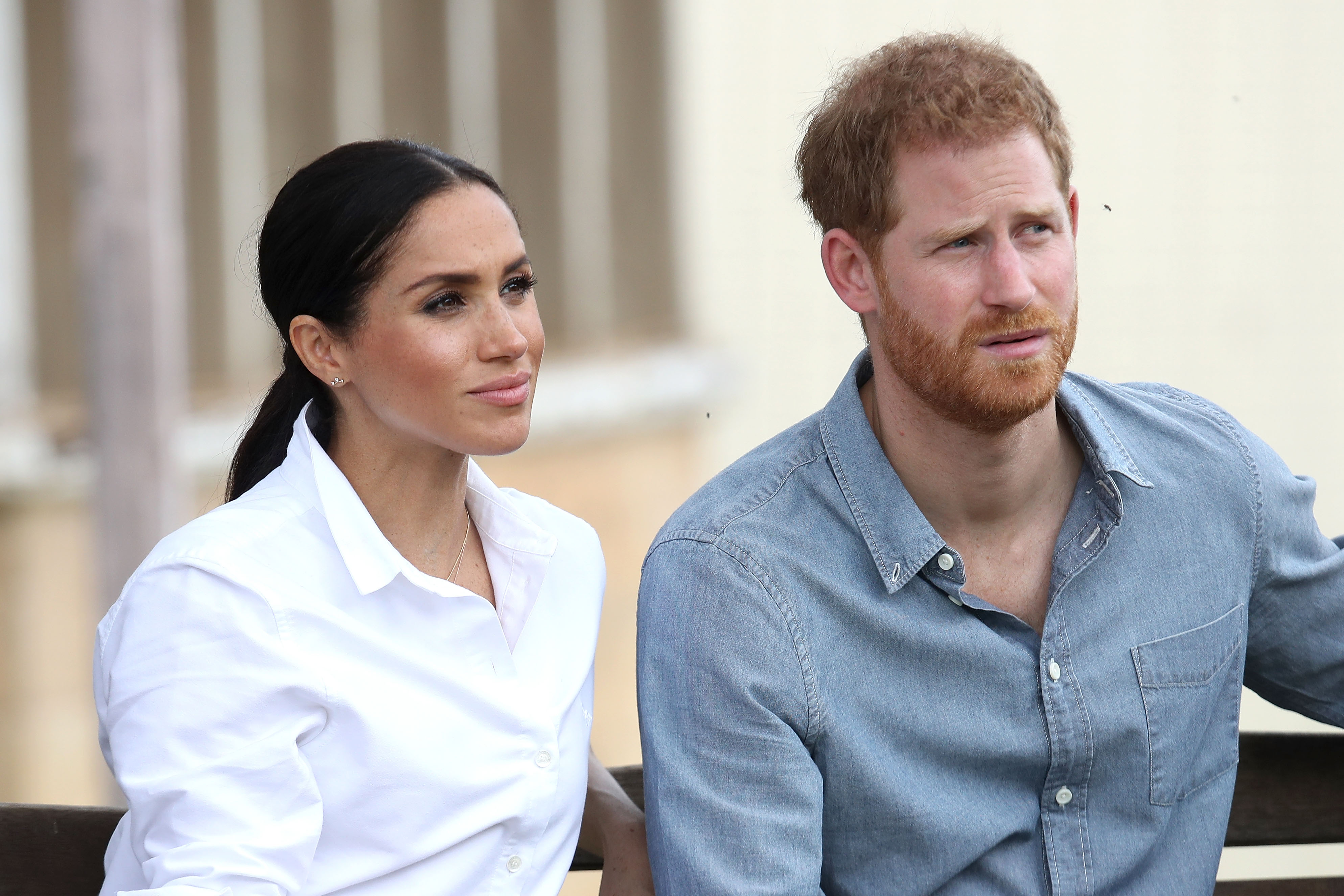 Meghan Markle wears a white shirt as she sits next to Prince Harry wearing a blue shirt