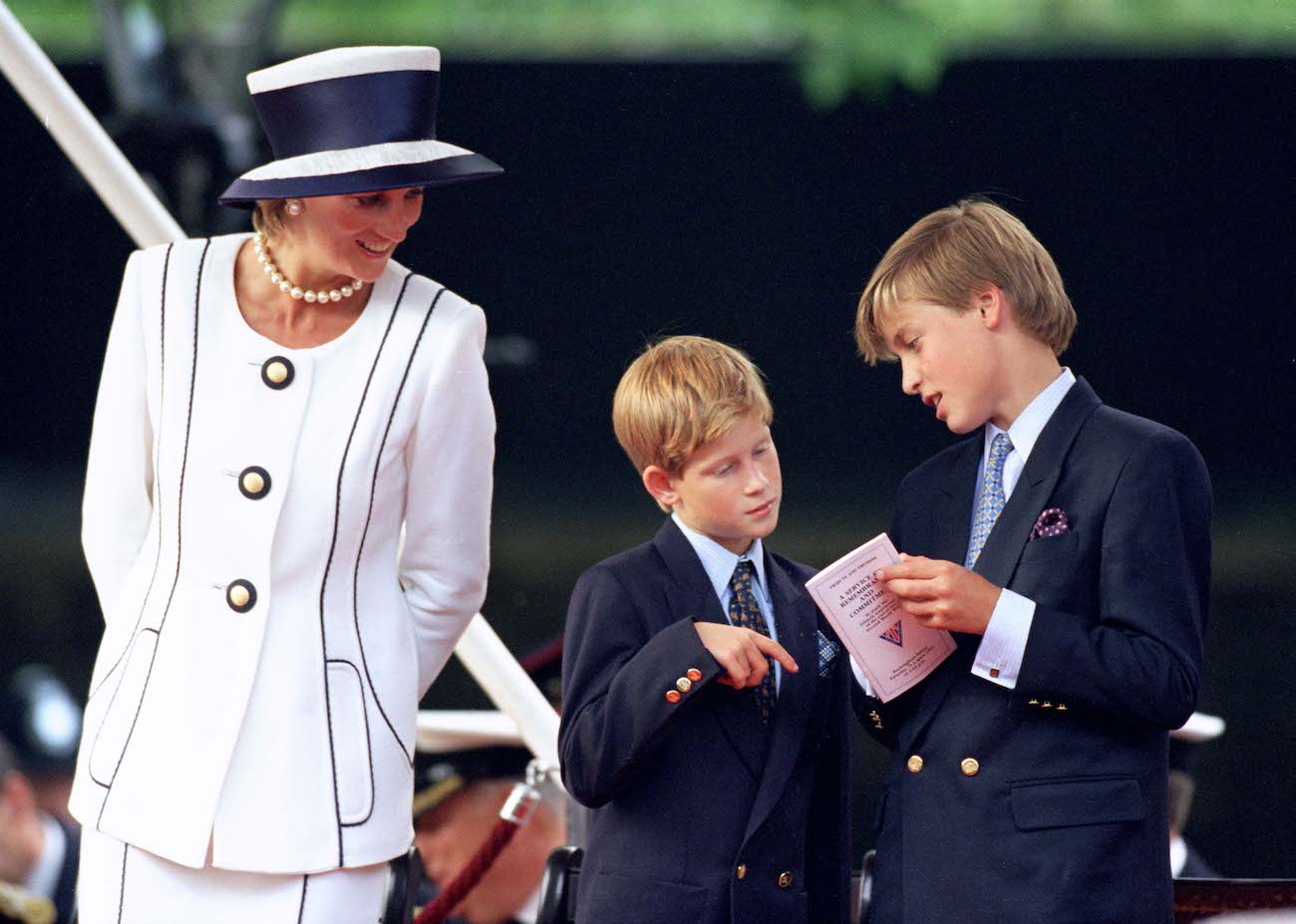 Princess Diana wearing a white outfit standing with Prince Harry and Prince William, who are wearing suits