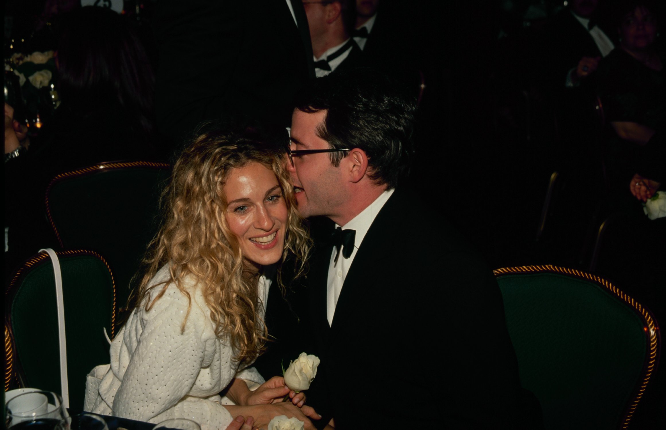 Sarah Jessica Parker smiling while her husband, Matthew Broderick, whispers in her ear at an event.