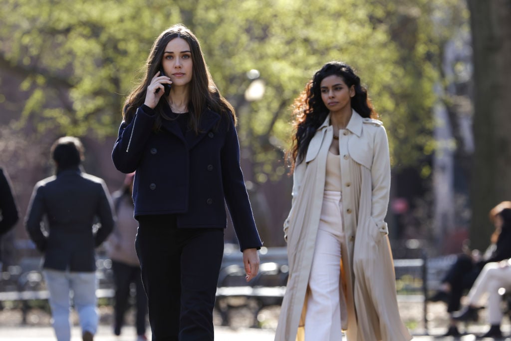  Megan Boone as Liz Keen walks as she talks on the phone. She is dressed in dark clothing while Rana Roy as Priya Laghari follows, dressed in ivory. 