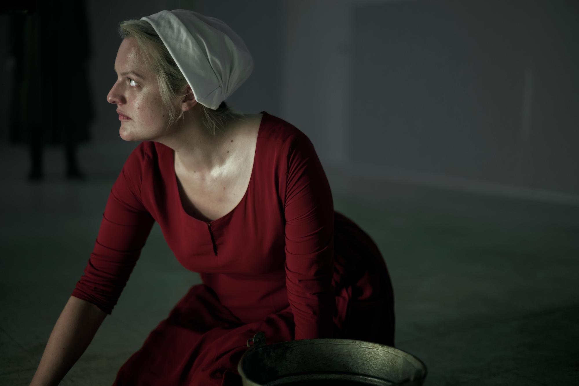 Elisabeth Moss as June, scrubbing a floor looking off camera