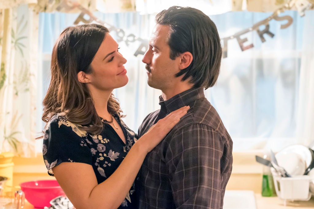 This Is Us Season 6 stars Mandy Moore as Rebecca, Milo Ventimiglia as Jack look loving at one another while standing in the kitchen.