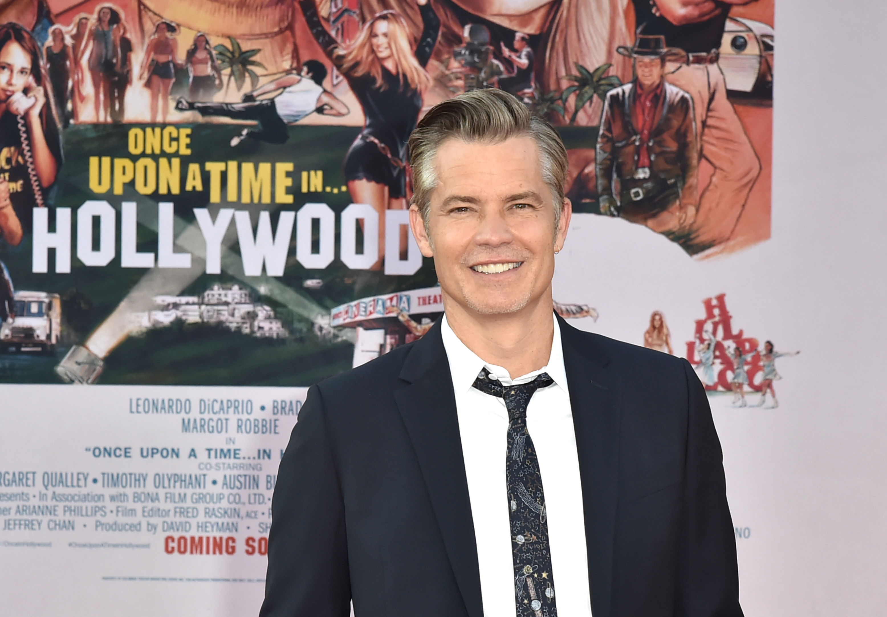 Timothy Olyphant stands in front of a Once Upon a Time in Hollywood poster