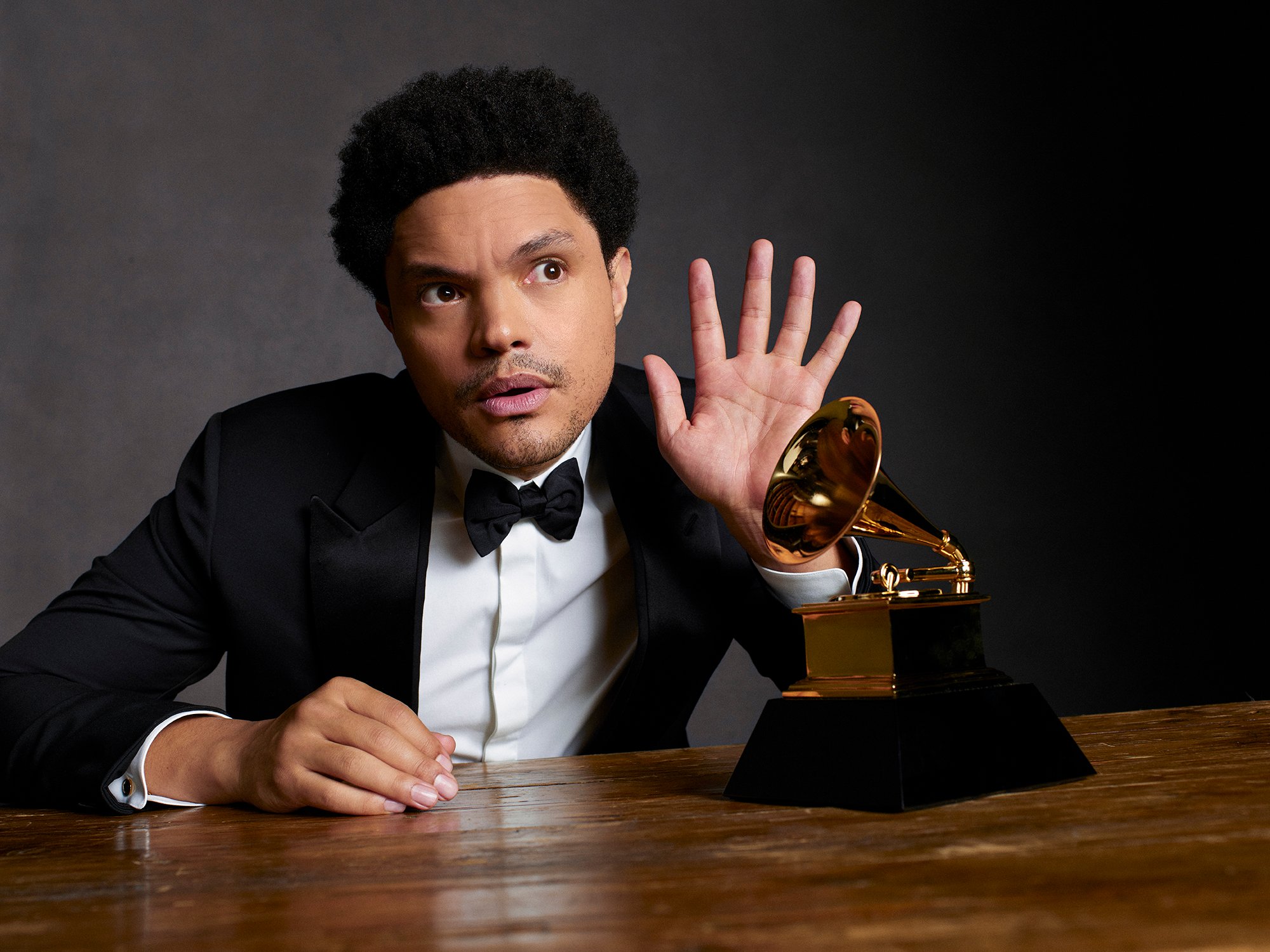Trevor Noah posed next to a Grammy Award with one hand up