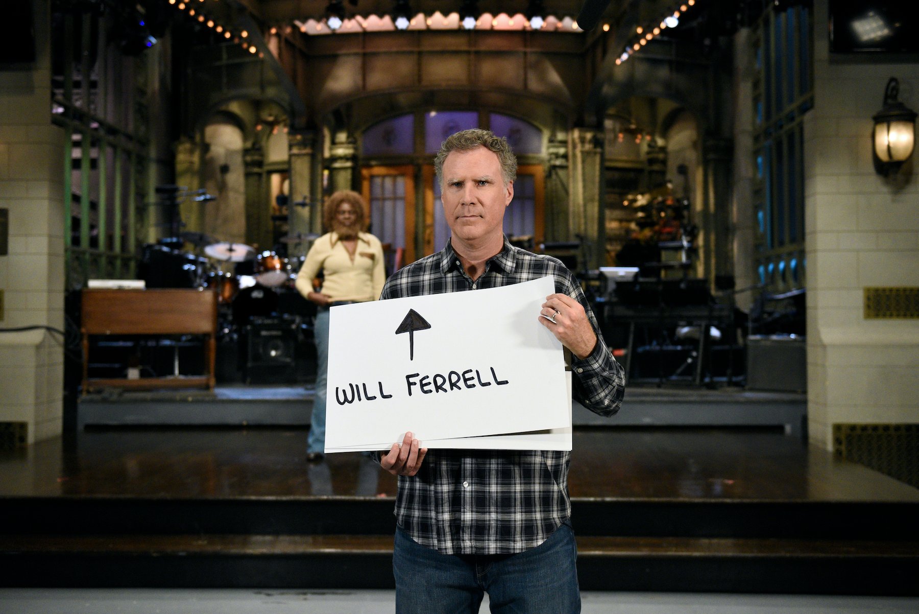 Will Ferrell on the 'SNL' stage holding a sign that says 'Will Ferrell'