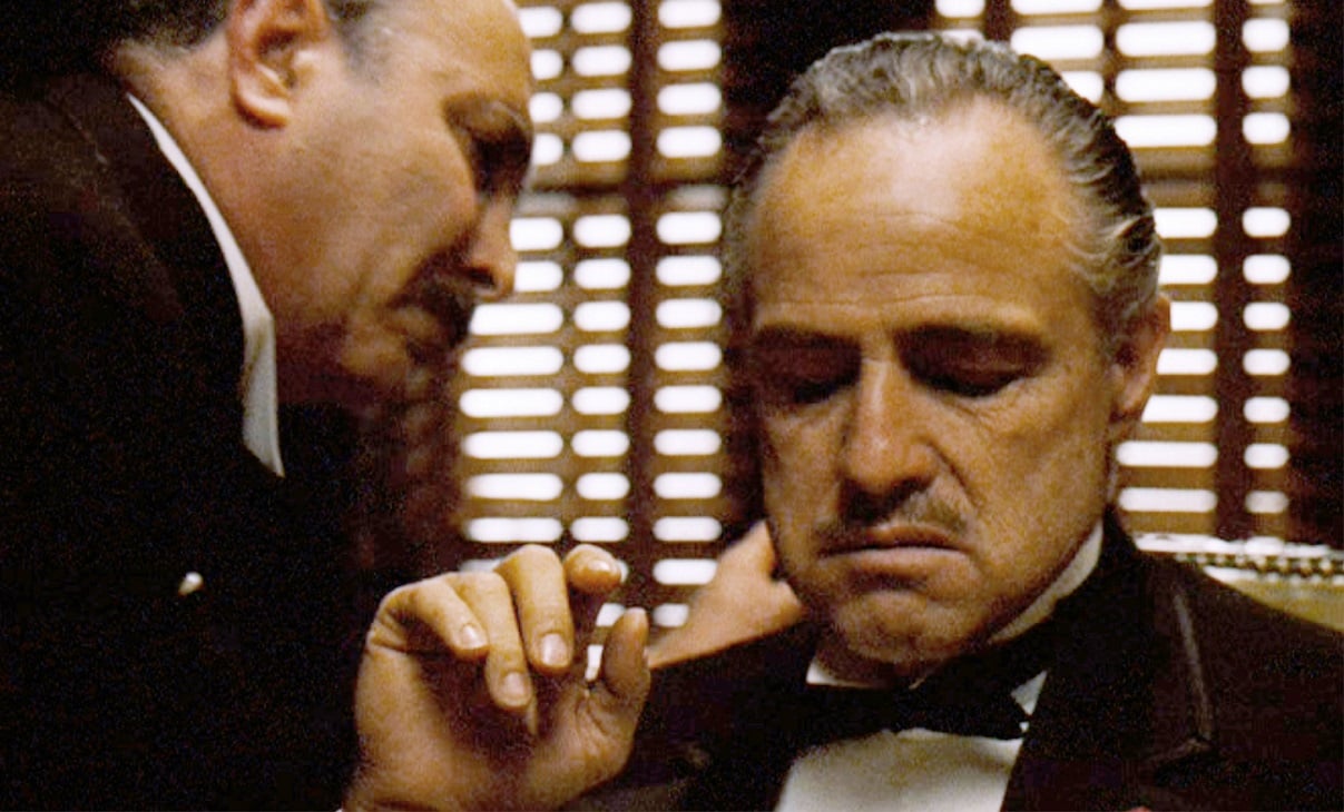 Salvatore Corsitto speaks in the ear of a seated Marlon Brando in a scene from 'The Gpdfather.'