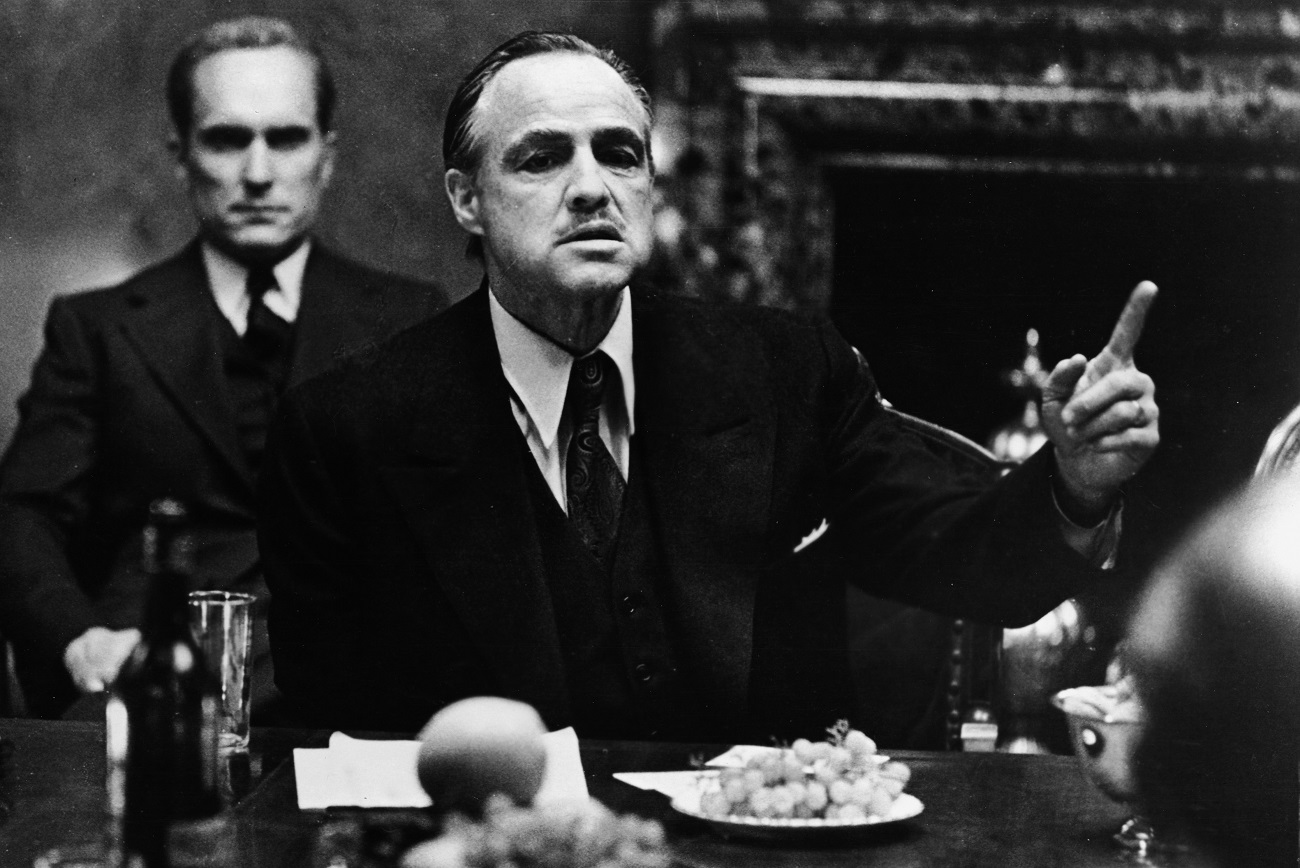 Marlon Brando gestures at a table while Robert Duvall sits behind him in 'The Godfather.'