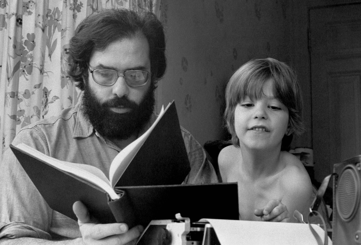 Francis Ford Coppola reads a book seated next to his young son.