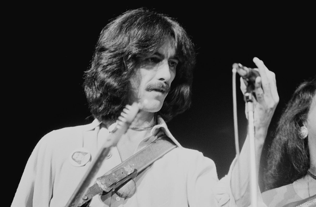George Harrison adjusts a microphone on stage in 1974.