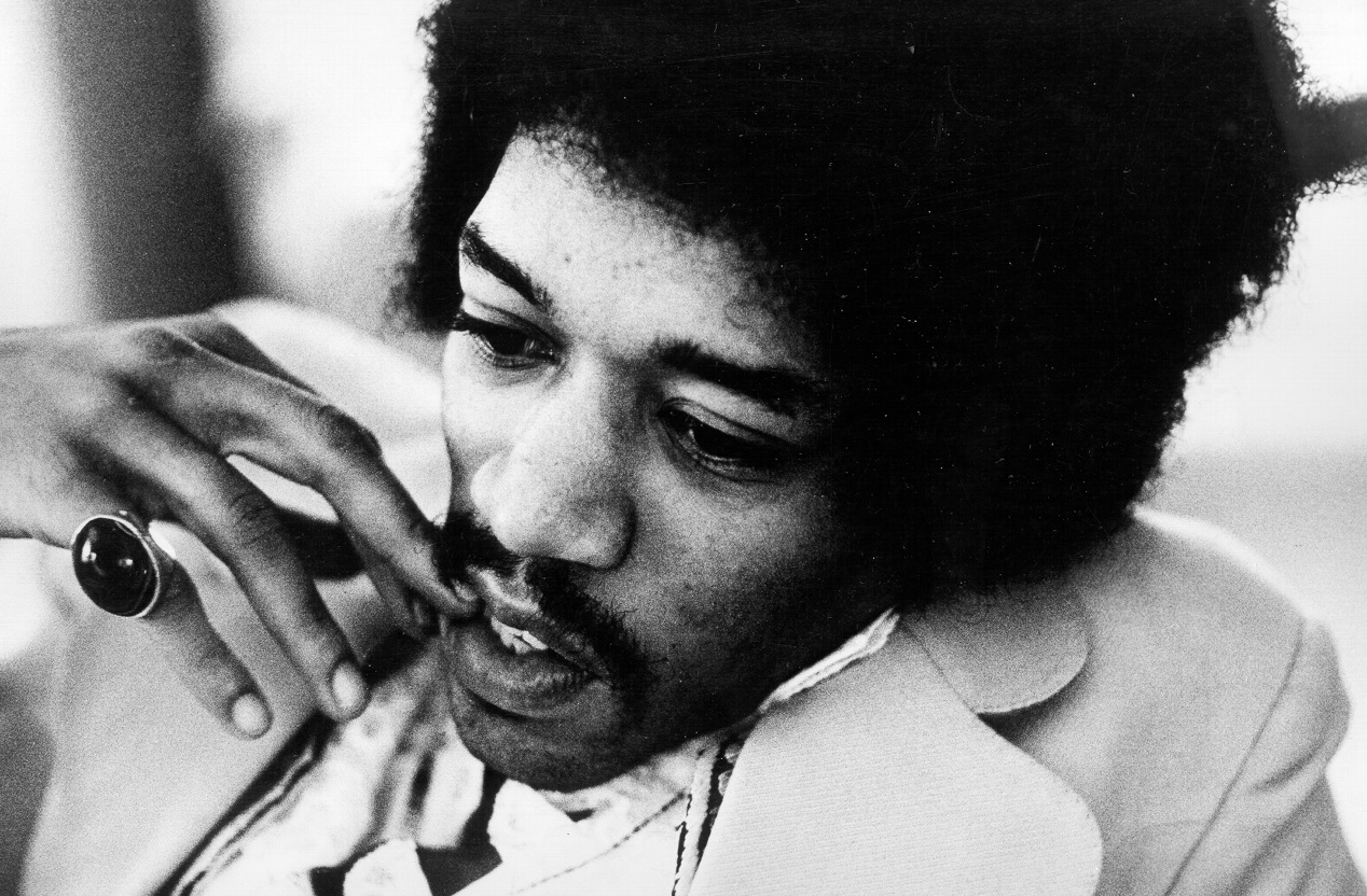 Jimi Hendrix holds his fingers to his face as he stares off-camera