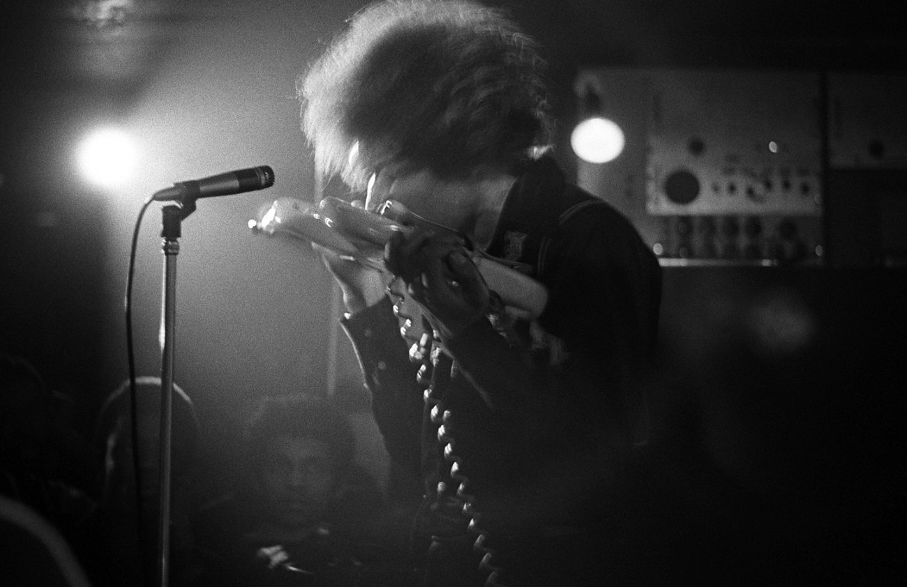 Jimi Hendrix playing the guitar with his teeth on stage in a dark London club