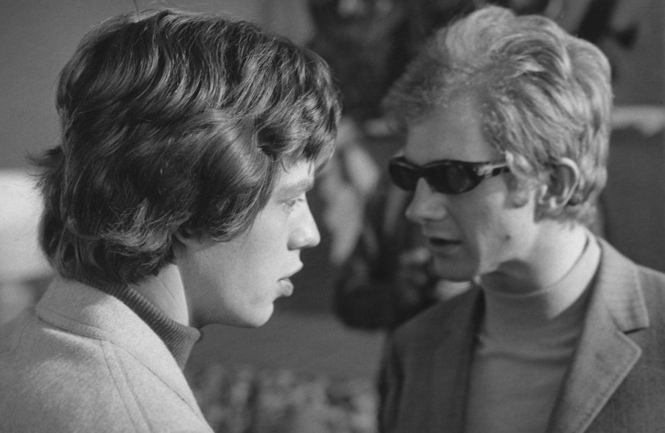 Mick Jagger seen in profile with Andrew Loog Oldham in the background